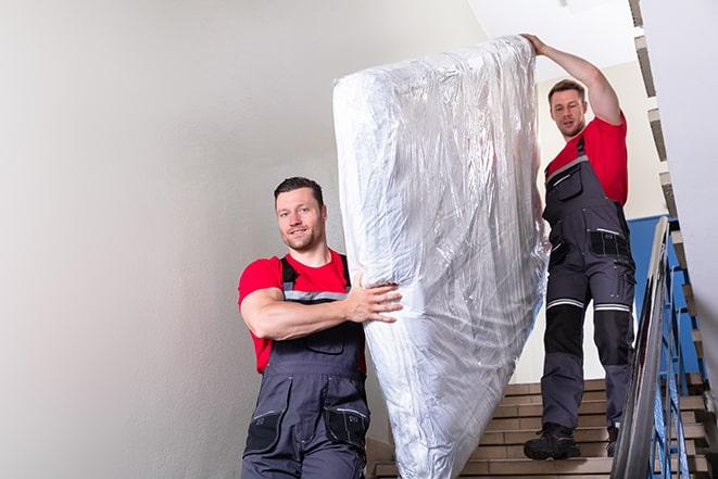 two workers safely transporting a box spring out of a house in Underwood